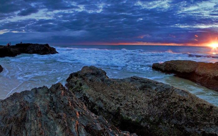 Sunset over ocean with rocky shore and waves