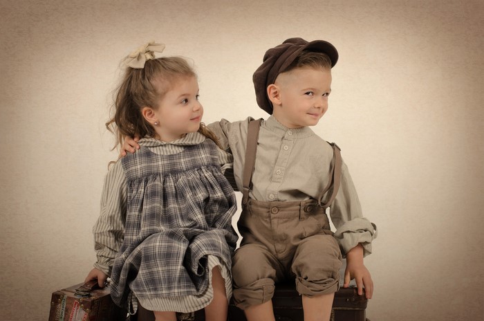 Boy and girl in vintage clothing sitting on suitcases