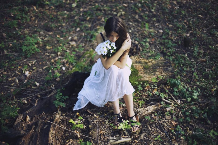 Brunette girl with bouquet sitting in forest