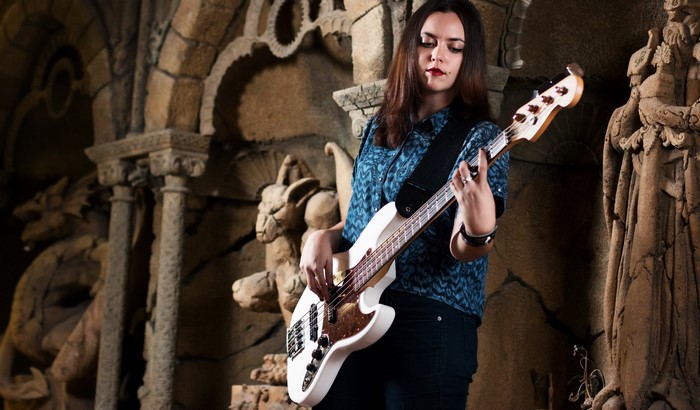 Woman playing a white bass guitar in a gothic setting