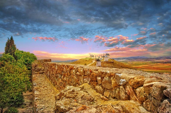 Stone wall with windmills on a hill at sunset