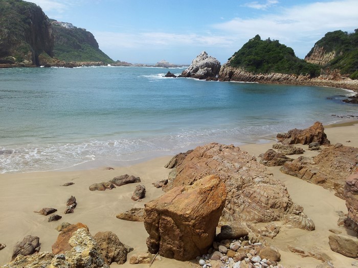 Beach with rocky outcrops and green hills in Knysna, South Africa