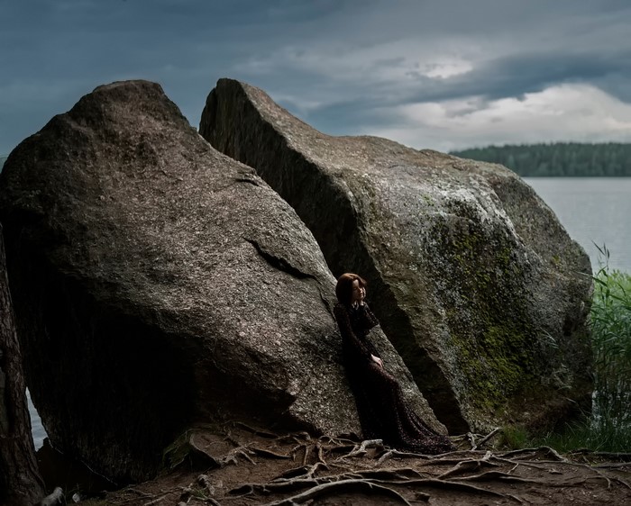 Woman leaning on large rocks by a lake