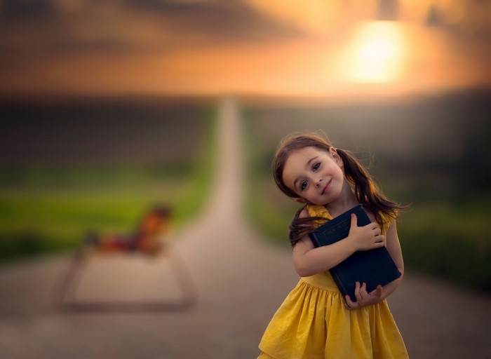 Girl holding a book on a road at sunset