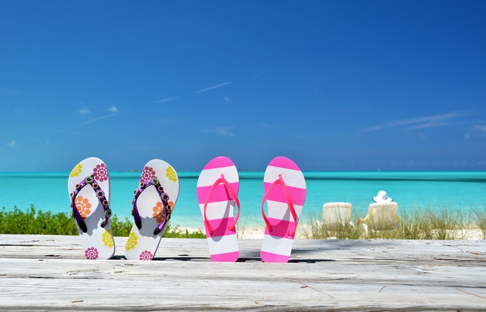 Four pairs of flip-flops on a wooden deck by the sea