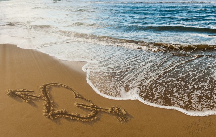 Heart with arrow drawn in sand on beach with ocean waves