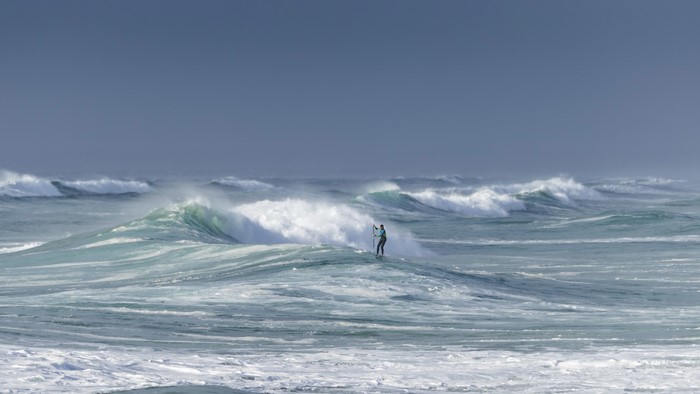 Person paddleboarding on large ocean waves