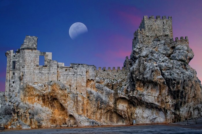 Castle ruins on a rocky crag under a moonlit sky