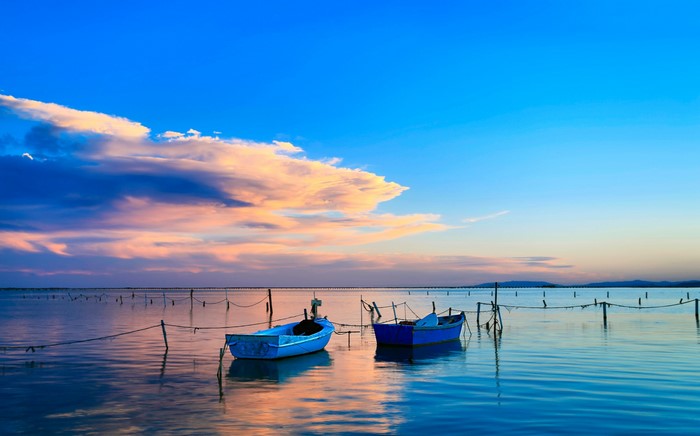Two blue boats on a calm sea at sunset