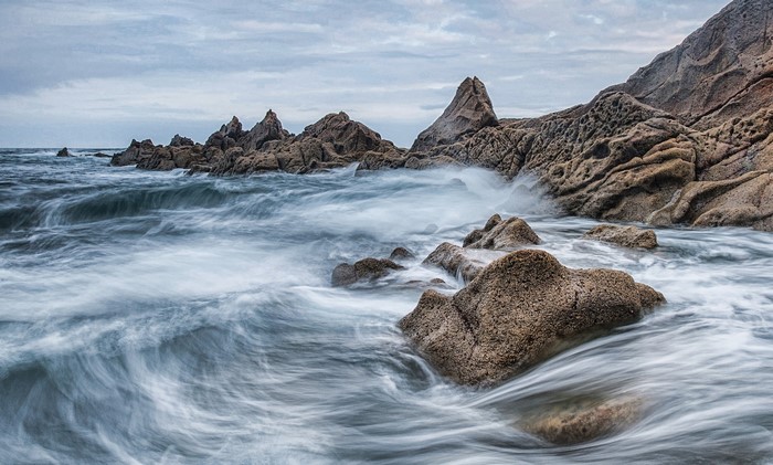 Waves crashing on rocky shore under cloudy sky