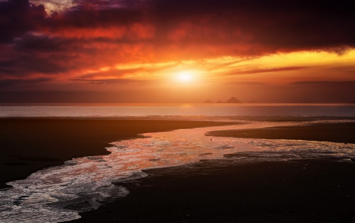 Sunset over the ocean with a stream on the beach