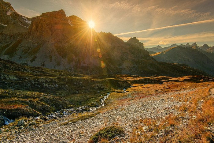 Sun setting over rocky mountains and a stream