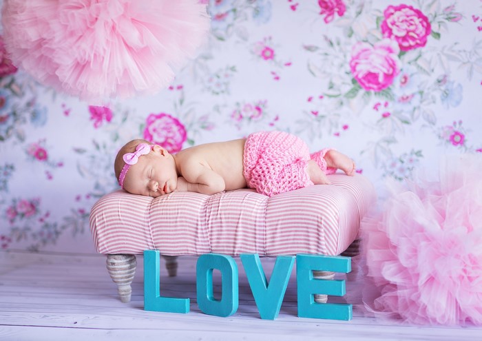 Newborn baby sleeping on a pink striped ottoman with 'LOVE' letters