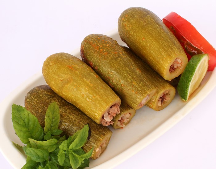 Stuffed zucchini with meat and rice, garnished with mint, lime, and tomato