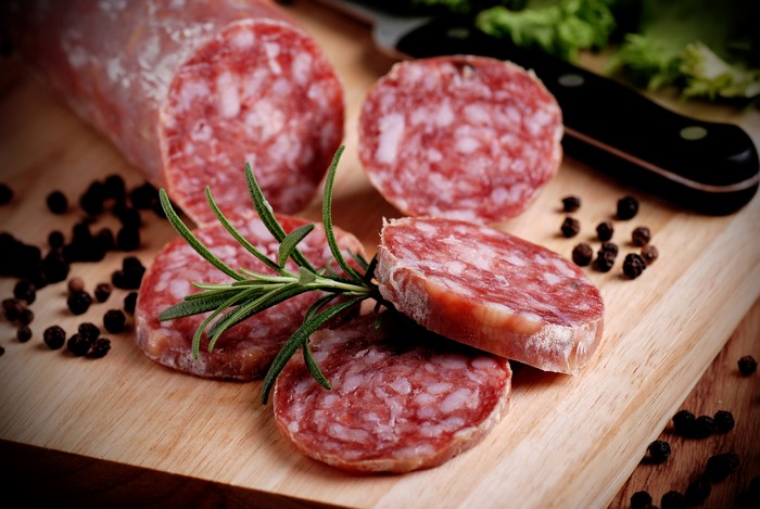 Sausage slices with rosemary and peppercorns on a cutting board