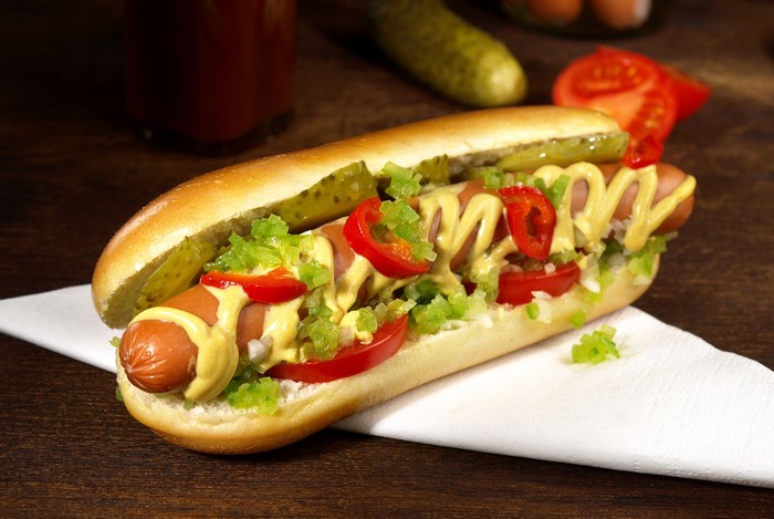 Hot dog with mustard, pickles, tomatoes, and peppers