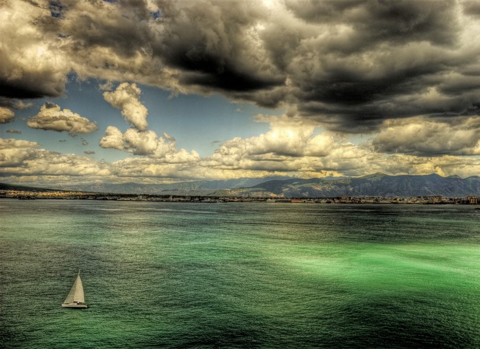 Sailboat on the sea with clouds and mountains