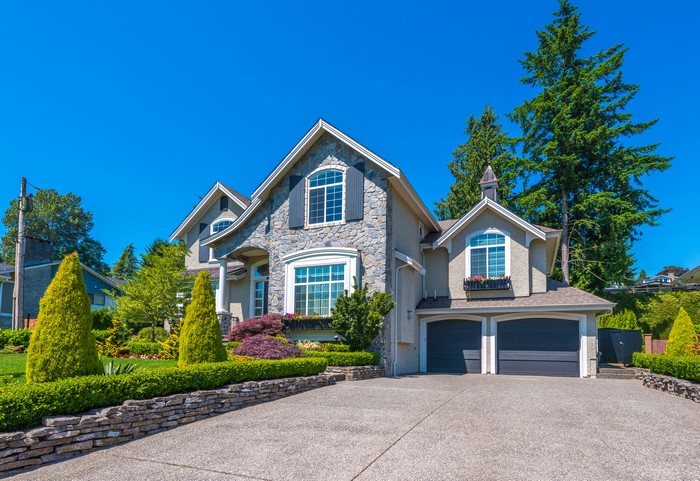 Luxury stone mansion with manicured gardens and driveway