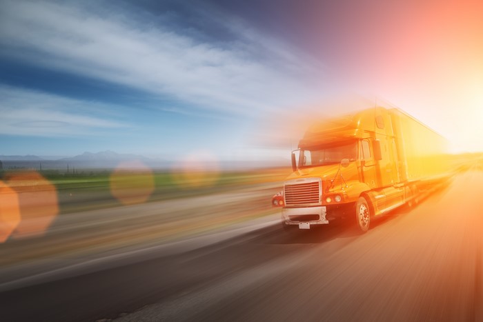 Orange semi-truck driving on a highway with motion blur