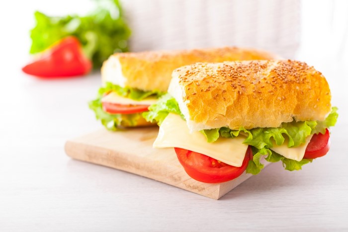 Two sandwiches with cheese, lettuce, and tomato on a wooden board