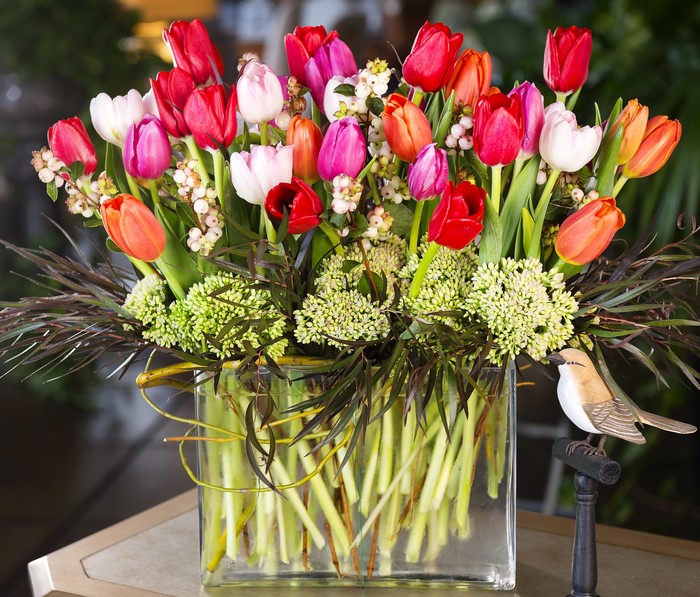 Colorful tulips in a glass vase with a bird figurine