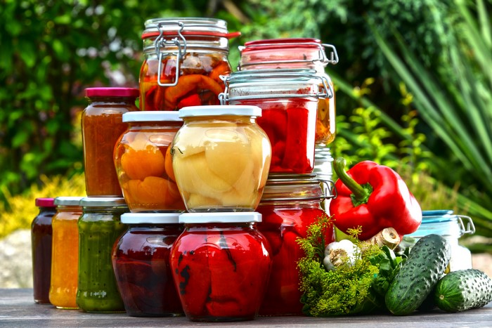Jars of preserved vegetables and fruits with fresh produce