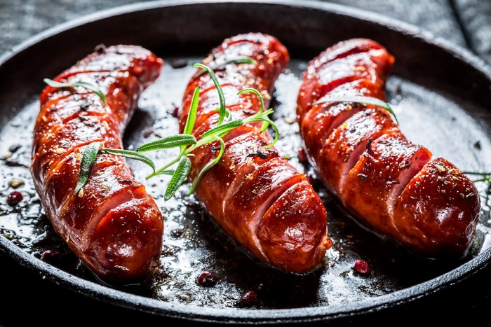 Three grilled sausages with rosemary in a pan