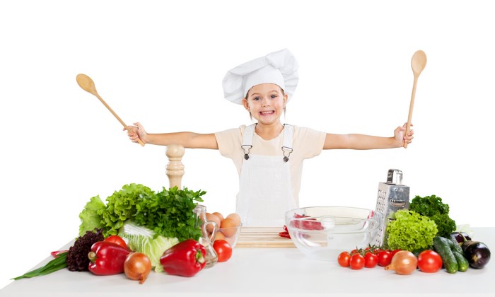 Little girl in chef hat with vegetables and spoons