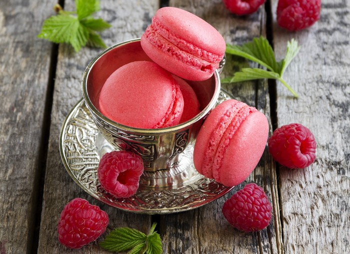 Pink raspberry macarons in a silver cup with fresh raspberries