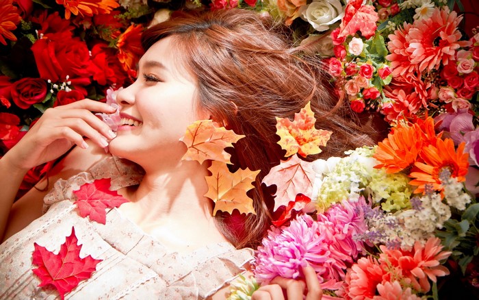 Asian woman lying among flowers with autumn leaves