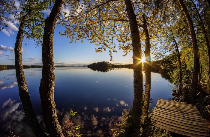 Sunset over a calm lake with trees and a wooden pier