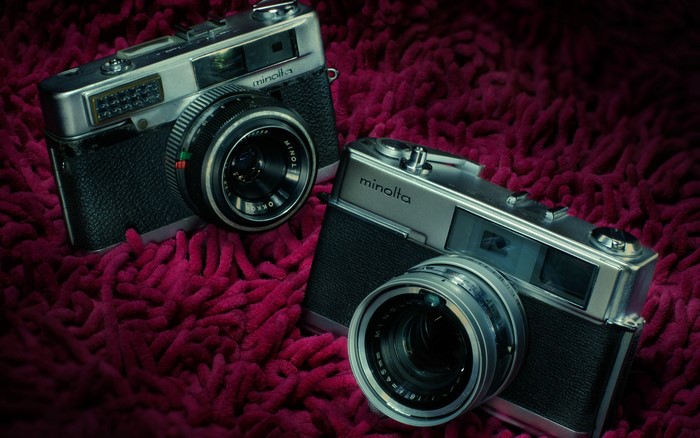 Two retro Minolta cameras on a textured surface