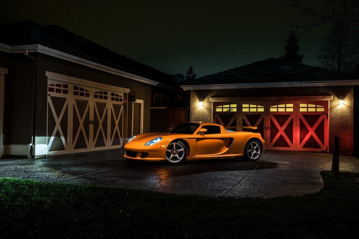Orange Porsche Carrera GT parked in front of garage at night