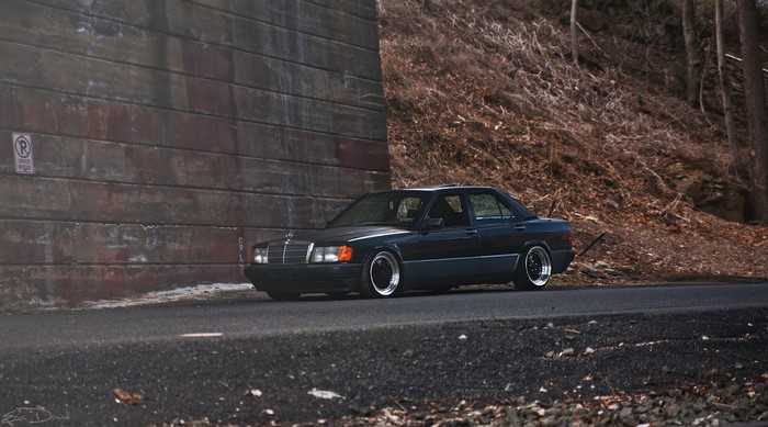 Black Mercedes-Benz 190E parked by a concrete wall