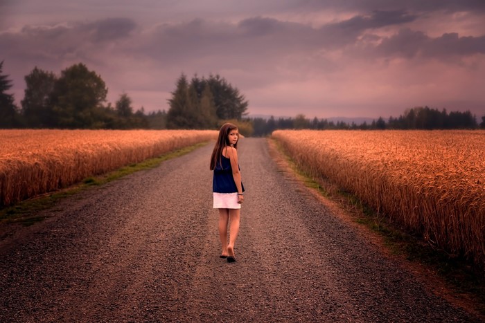 Girl walking on a road between wheat fields