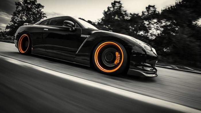 Black Nissan GT-R with orange rims driving on a road