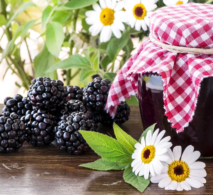 Blackberry jam in a jar with blackberries and daisies