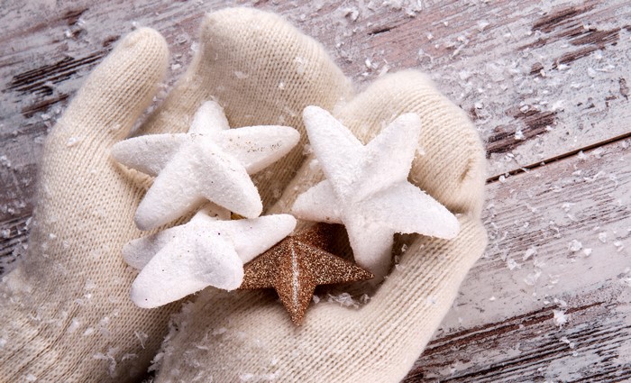 Hands in mittens holding star ornaments with snow