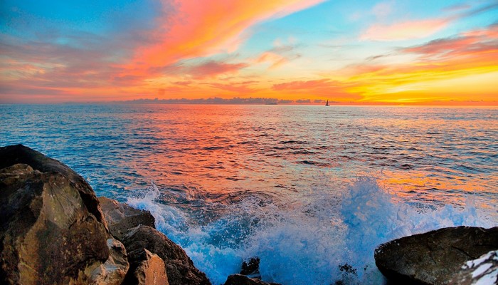 Sunset over the ocean with waves crashing on rocks