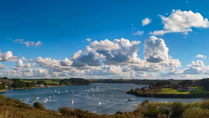 Boats on a wide river under a cloudy blue sky
