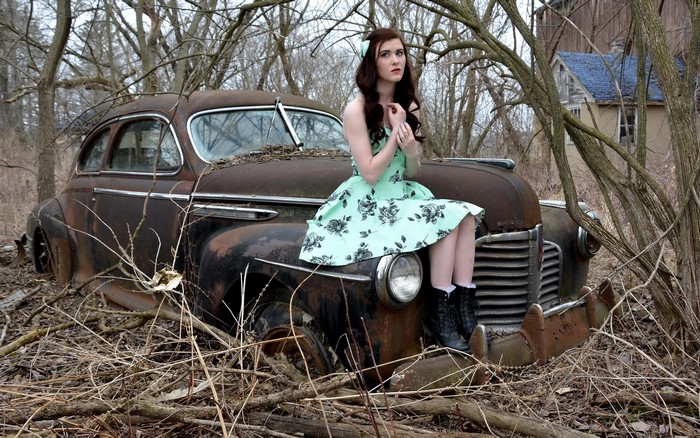 Woman in retro dress sitting on abandoned car