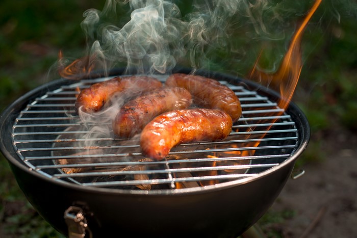 Sausages grilling over a fire with smoke and flames