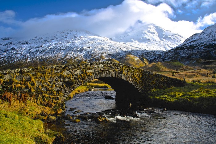 Stone bridge over a river with snow-capped mountains