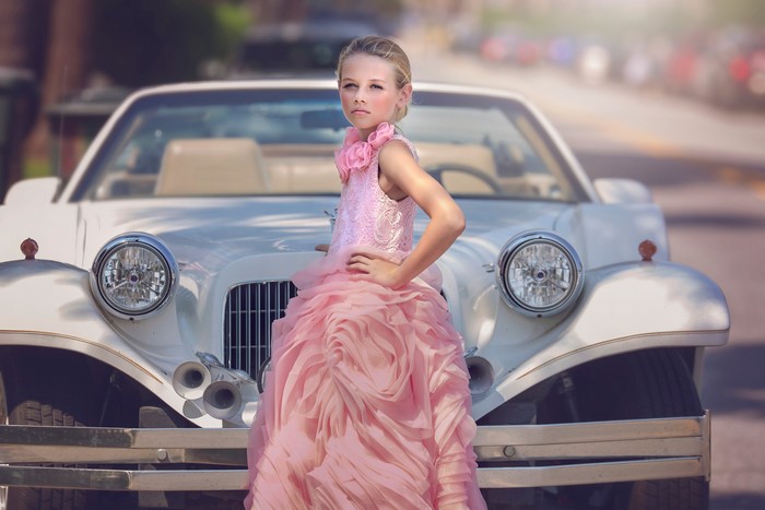 Girl in pink dress posing by a white limousine