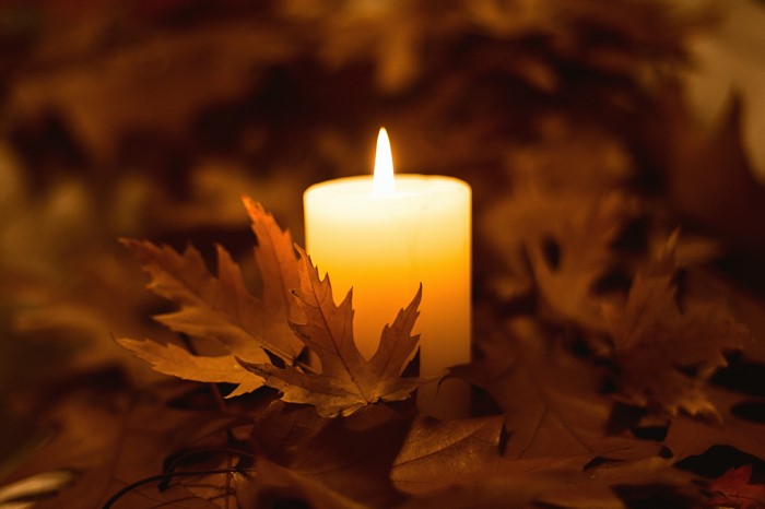 Lit candle surrounded by autumn leaves