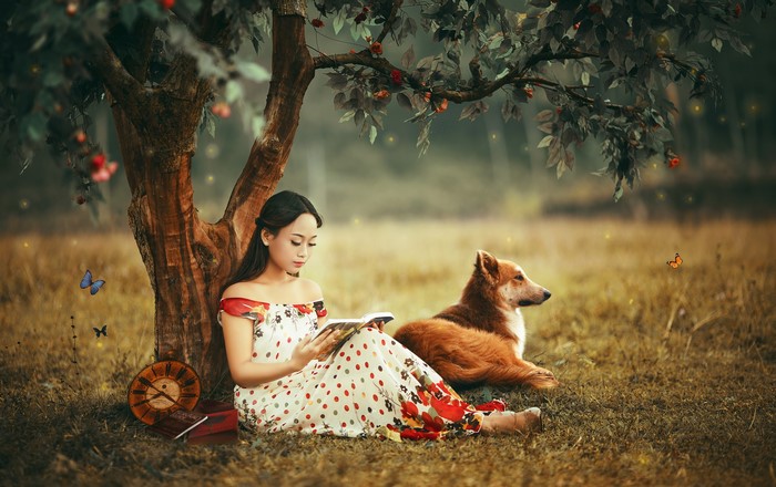 Asian woman reading under a tree with a dog