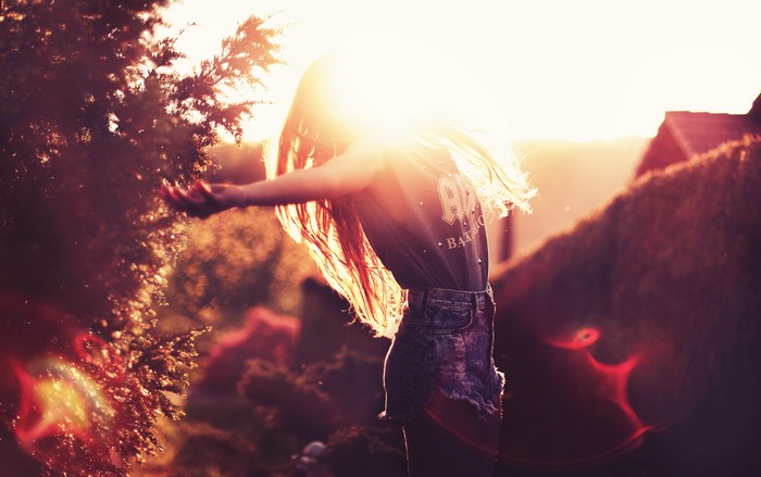 Girl in denim shorts with arms outstretched at sunset