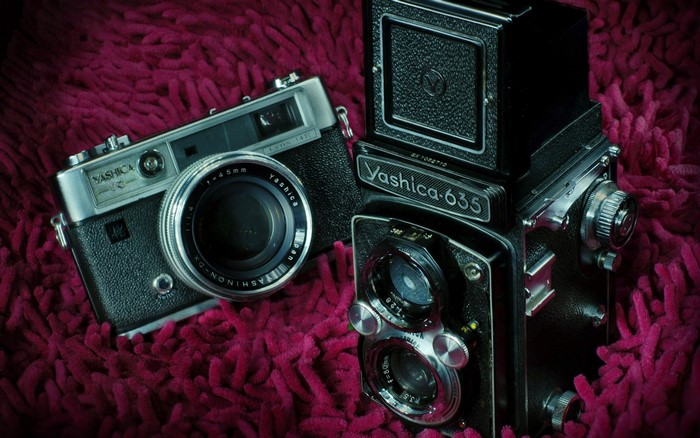 Two vintage Yashica cameras on a textured surface