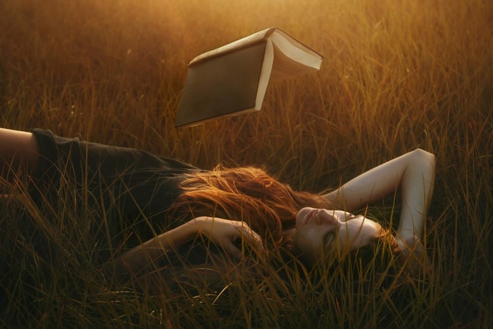 Woman lying in grass with levitating book