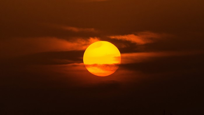 Sun partially obscured by clouds at sunset